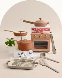 Ceramic cookware set with pots, pans, and kitchen tools on a neutral background