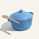 A blue Ceramic Nonstick Perfect Pot 6 L, designed for family-sized meals and featuring two handles, sits on a light surface with a wooden spoon resting on top.