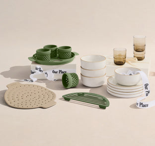 Collection of ceramic and glass tableware with 'Our Place' branding on a beige background