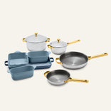 Titanium Pro Cookware + Bakeware Set 2.0 featuring high-performance silver pots and pans with gold handles paired with blue ceramic bakeware dishes.