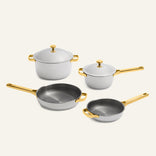 Titanium Pro Cookware Set 2.0 featuring two white pots with lids and two gray frying pans, all with gold-toned handles and knobs, shown as a collection of non-toxic, stainless steel cookware.
