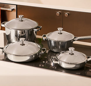 Set of stainless steel pots and pans with lids on a stove