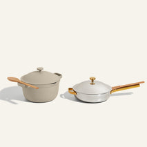 A beige covered pot with a wooden spoon and a white covered skillet with a wooden handle and knob are placed side by side on a light background.