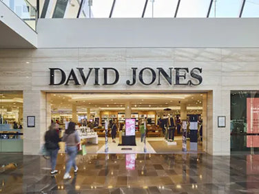 Exterior view of a David Jones department store in a shopping mall, with several people walking in and out of the entrance and store displays visible inside.