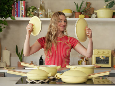 Woman in a kitchen holding yellow kitchen items with a shelf of books and decor in the background.