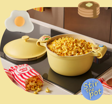 Yellow pot with popcorn on a stove, surrounded by a carton of popcorn and an egg-shaped container.