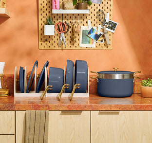 Kitchen counter with pots, pans, and a pegboard with tools and decor on an orange wall.
