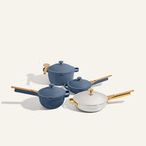 The Titanium & Ceramic Cookware Set, featuring two blue Perfect Pot line pots with lids, a blue frying pan, and a white frying pan—all with wooden handles—is arranged on a light background.