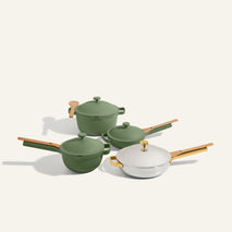 Four pieces from the Titanium & Ceramic Cookware Set, each with wooden handles, are arranged on a light background; three are green and one is white with a gold knob.