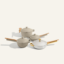 The Titanium & Ceramic Cookware Set includes four pieces with beige and white finishes and light wooden handles, inspired by the Always Pan, displayed against a plain light background.
