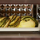 Three braided pesto dough rolls on a baking sheet inside an oven.