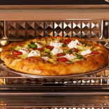 Pizza topped with zucchini, tomatoes, artichokes, and dollops of cheese baking in an oven.