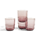 Four pink glass tumblers are arranged in a staggered stack on a white surface with a plain light background.