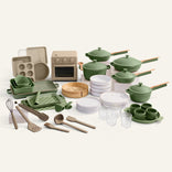 A set of green cookware, white plates, and a cream oven on a white background