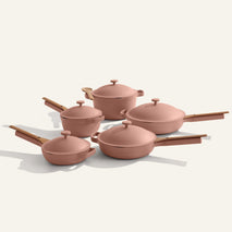 The Cookware Set+ is a stylish pink ceramic nonstick cookware collection with wooden handles, including assorted pots and pans with matching lids, all showcased on a light background.