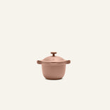 The Petite Perfect Pot, featuring a matte pink finish, two handles, and a lid, sits centered on a plain light background.