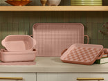 Set of pink ceramic cookware with checkered patterns on a kitchen counter.