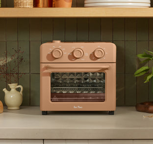 A tan Our Place countertop oven with three front-facing control dials sits on a kitchen counter.