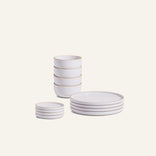 The Plates & Bowls Set includes four handcrafted ceramic bowls, four small plates, and four large plates with thin gold rims, displayed on a plain light background.