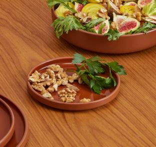 A brown plate with walnuts and parsley sits beside a larger bowl containing salad with figs, greens, yellow beet slices, and walnuts on a wooden table.