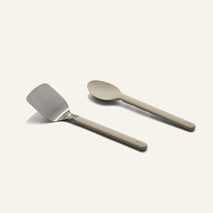 A stainless steel spatula and a tan serving spoon from a Titanium Pro Utensil Set.