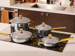 Set of silver cookware with gold handles on a stove in a kitchen setting