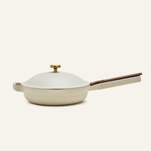 The Always Pan 2.0, a bestselling beige nonstick pan, features a matching domed lid with a gold knob and long angled handle, shown on a plain light background.