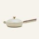 The ceramic nonstick always pan made without PFAS 2.0, a beige nonstick frying pan from a bestselling cookware set, comes with a matching domed lid, wooden handle, and brass knob, shown against a plain light background.