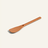A wooden spatula with a flat, angled edge and a small hole in the center, placed on a plain light background.