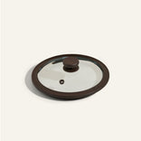 A round glass pot lid with a brown handle and rim is shown on a plain light background.