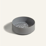 A round, gray container with a perforated insert, shown on a plain light background.