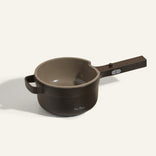 A dark brown saucepan with a long handle and a side grip, featuring a spout, is shown on a light background.
